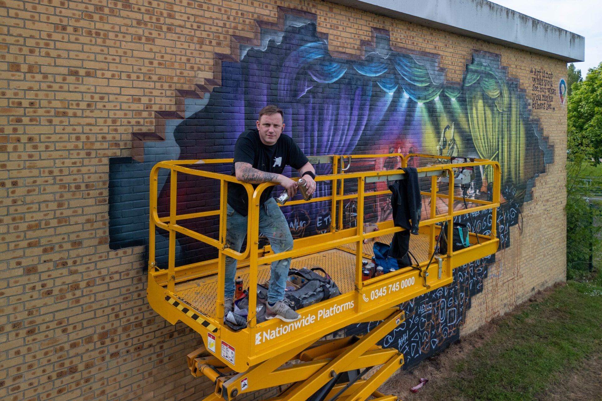 Nathan Murdoch, Artists completes an installation on the wall of the Key Theatre showing people looking through the wall to the wonders inside. - News for Peterborough and Cambridgeshire News for Peterborough and Cambridgeshire - Nathan Murdoch working on a mural on the wall of the Key Theatre, Peterborough.  Embankment, Peterborough Wednesday 08 May 2024. Picture by Terry Harris.