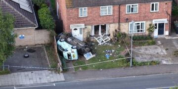 Emergency services at the scene in Paston Ridings, Peterborough, after a car crashed into a semi-detached house and overturned beside a parked vehicle.