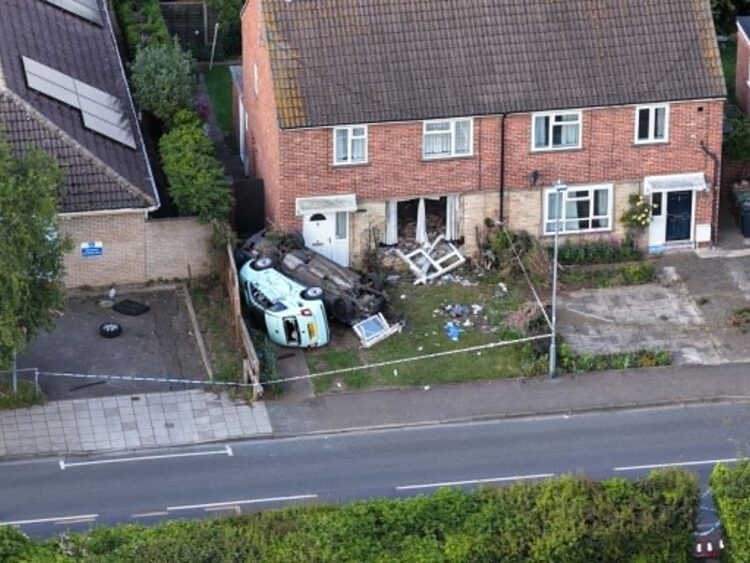 Emergency services at the scene in Paston Ridings, Peterborough, after a car crashed into a semi-detached house and overturned beside a parked vehicle.